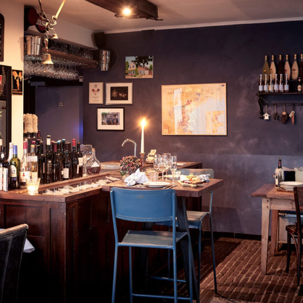 Het restaurant van Gasterie Lieve Hemel, met een houten tafel met blauwe stoelen, wijnflessen, een brandende kaars