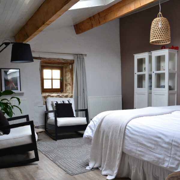 Een gastenkamer, met stoeren balken, witte kast, wit bed en twee fauteuils, landelijke stijl