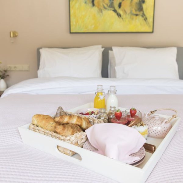 Tweepersoons bed met zacht roze sprei en wit dienblad met ontbijt lekkers