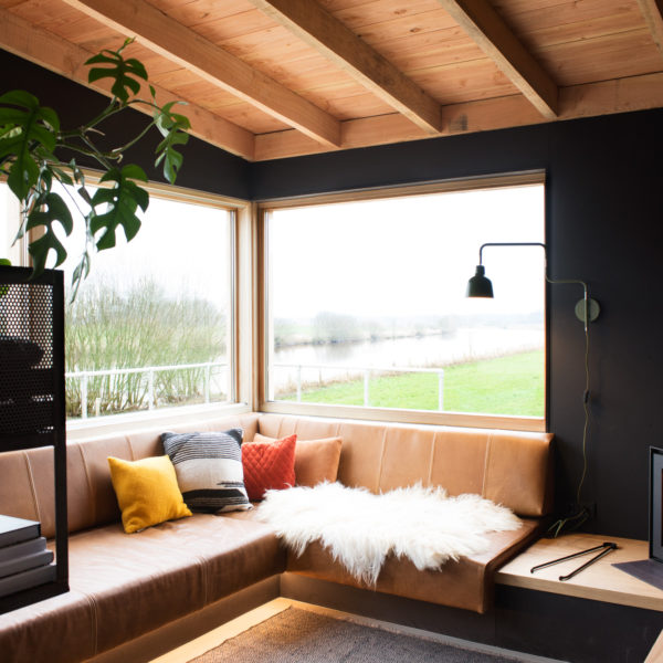 De woonkamer met loungehoek, houtkachel en grote ramen met uitzicht over de Vecht.
