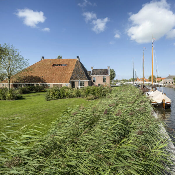 Grote Friese boerderij aan het water met bootjes aan de steiger