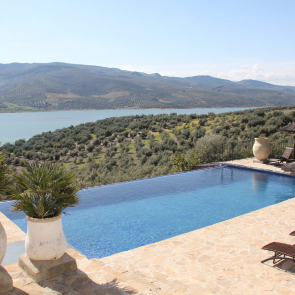 Infinity pool met ligbedden en rieten parasols, uitzicht over heuvels en meer