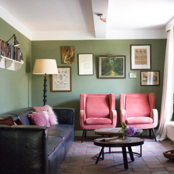 Woonkamer met roze fauteuils, een hangbank en groene muren