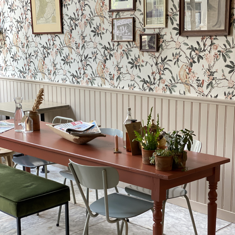 Houten tafel met planken en bloemetjesbehang op de achtergrond.