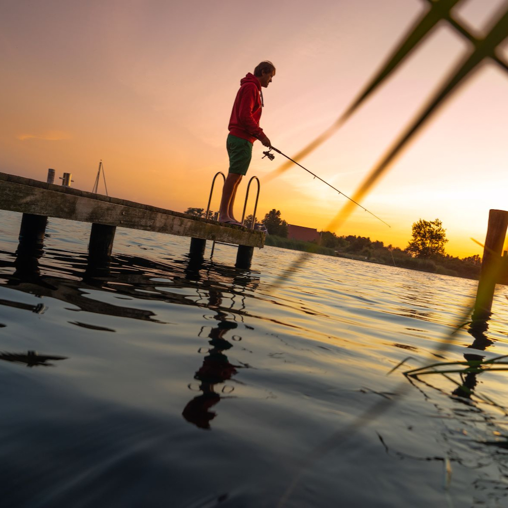 Visser op een steiger aan de waterkant bij zonsondergang.